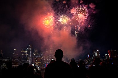 Personas observan cómo los fuegos artificiales iluminan el horizonte de Manhattan