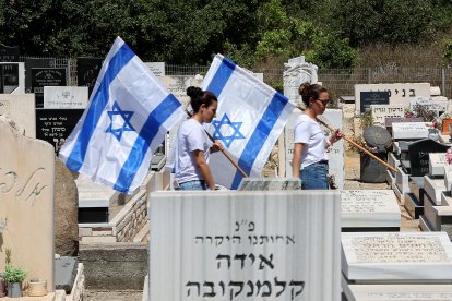 Two women carry the Israeli flag amid graves at a cemetary during the funeral of an Israeli soldier killed in the Gaza Strip
