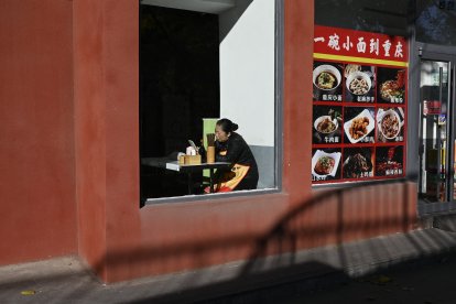Una empleada usa su teléfono móvil mientras espera a los clientes en un restaurante de Pekín