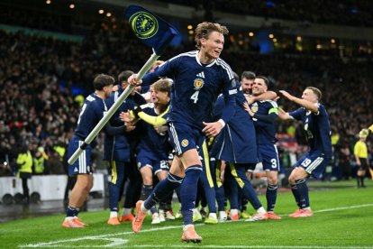 Scotland's midfielder #04 Scott McTominay grabs the corner flag as Scotland's midfielder #23 Kenny McLean celebrates with teammates after scoring his long-range last-kick of the game goal during the FIFA World Cup 2026 European qualification football match between Scotland and Denmark at Hampden Park in Glasgow on November 18, 2025. Scotland scored two dramatic stoppage-time goals to beat 10-man Denmark 4-2 on Tuesday and reach the World Cup for the first time since 1998. (Photo by ANDY BUCHANAN / AFP)