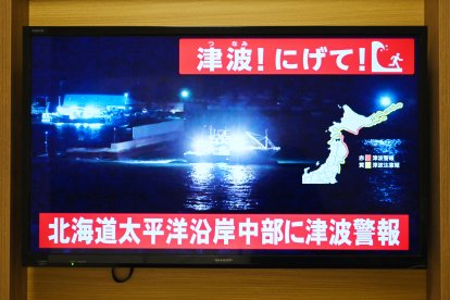 Un aviso que dice «¡Tsunami! ¡Corran!» (arriba) y «Se emite una alerta de tsunami para la costa pacífica central de Hokkaido» parpadea sobre las imágenes en directo de un barco que sale de un puerto, en una pantalla de televisión en Sapporo, en la prefectura de Hokkaido, al norte de Japón, el 8 de diciembre de 2025. Japón registró un tsunami de 40 centímetros (16 pulgadas) tras un terremoto de magnitud 7,6 el 8 de diciembre.