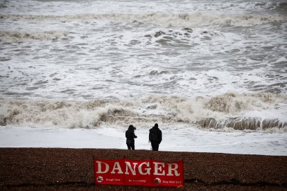 People look at the waves while standing behind a warning sign reading "Danger" (Files)