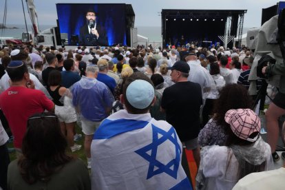 Una persona con la bandera de Israel y otras personas asisten a una ceremonia para conmemorar el Día Nacional de Reflexión por las Víctimas y los Sobrevivientes, en la playa de Bondi, Sídney, el domingo 21 de diciembre de 2025, tras el tiroteo ocurrido en Bondi el 14 de diciembre. (Foto AP/Mark Baker)