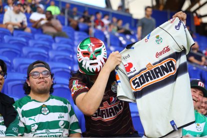 A fan of Santos Laguna wears a mask while holding up a jersey during a soccer match against Santos Laguna at Sports Illustrated Stadium in Harrison, New Jersey, on August 6, 2026. (Photo by Gordon Donovan/NurPhoto) (Photo by Gordon Donovan / NurPhoto via AFP)