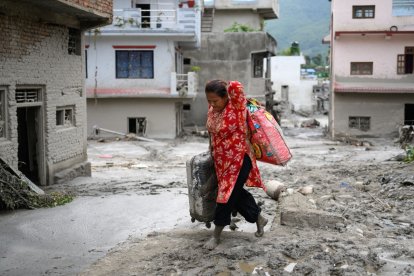 A woman salvages her belongings from her house heavily covered in mud following flash floods at Devighat in Nepals Nuwakot district on August 28, 2026. More than 1,400 people are missing and at least 552 have been killed after a devastating, tsunami-like wall of water gouged a path through the border region between Nepal and Tibet, sweeping away entire villages. (Photo by MANAN VATSYAYANA / AFP)