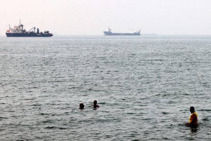 Men bathe in the Gulf waters as vessels in the background transit the Strait of Hormuz off the coast of Iran's southern port city of Bandar Abbas on September 7, 2026. Iran's top negotiator threatened on September 6 of a more forceful response to any further US attacks after Tehran targeted American warships in their latest round of clashes. The exchanges of fire, which began with US raids last week, come amid a deadlock in the six-month war between the two foes. (Photo by ATTA KENARE / AFP) /