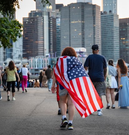 Una persona se envuelve con una bandera de Estados Unidos como una capa mientras la multitud se reúne para la celebración de los fuegos artificiales del 4 de Julio de Macy’s a lo largo del río Este