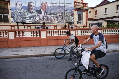 Two men in Cuba ride their bicycles in front of a propaganda of the regime.