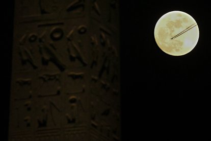 An airplane flies over the full moon, next to the Luxor Obelisks at the Place de la Concorde in Paris.