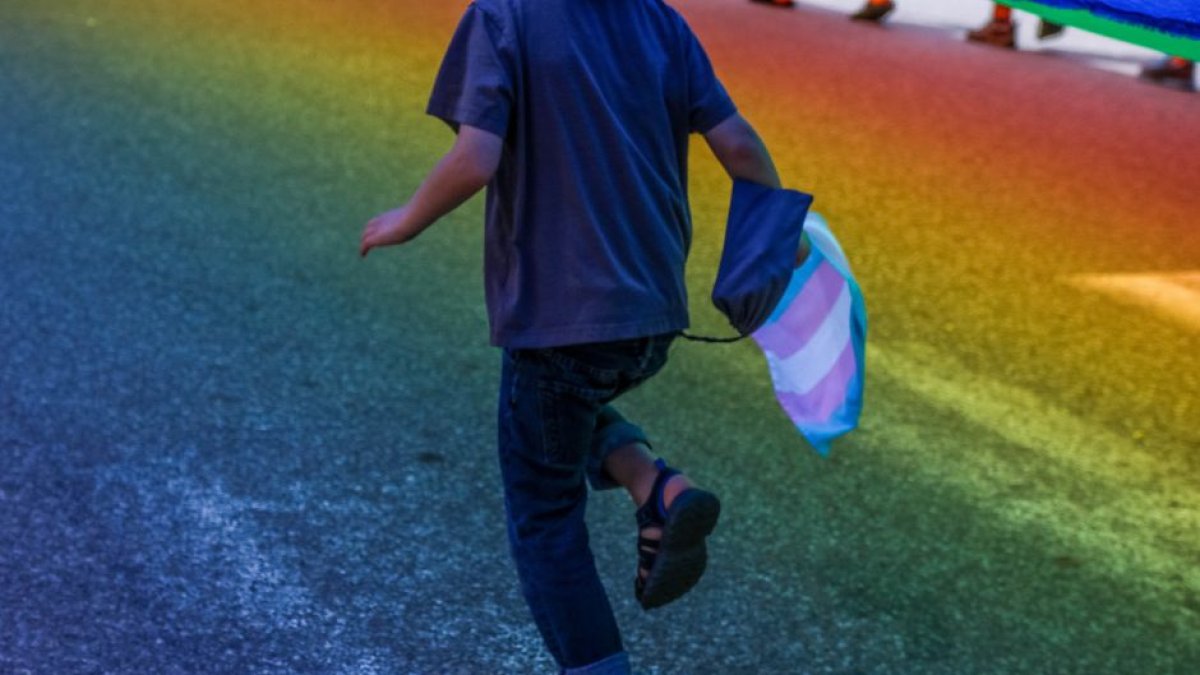 Imagen de archivo de un niño corriendo con la bandera trans en la mano.