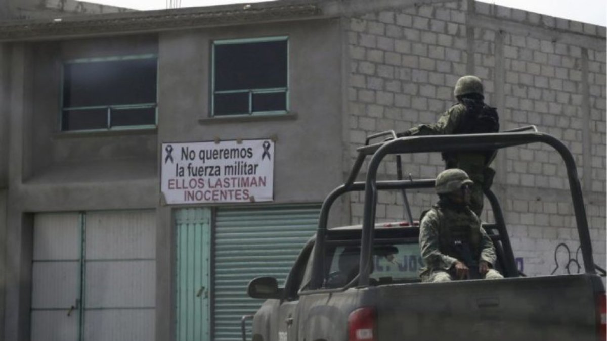 Militares sobre una pick-up patrullan las calles de una localidad mexicana. Al fondo, un cartel en contra de la presencia del Ejército.