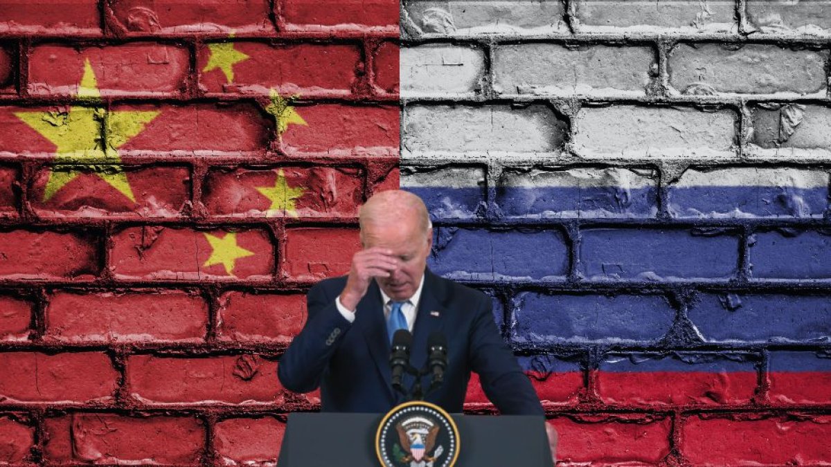 Biden sosteniéndose la cabeza delante de las banderas rusa y china.