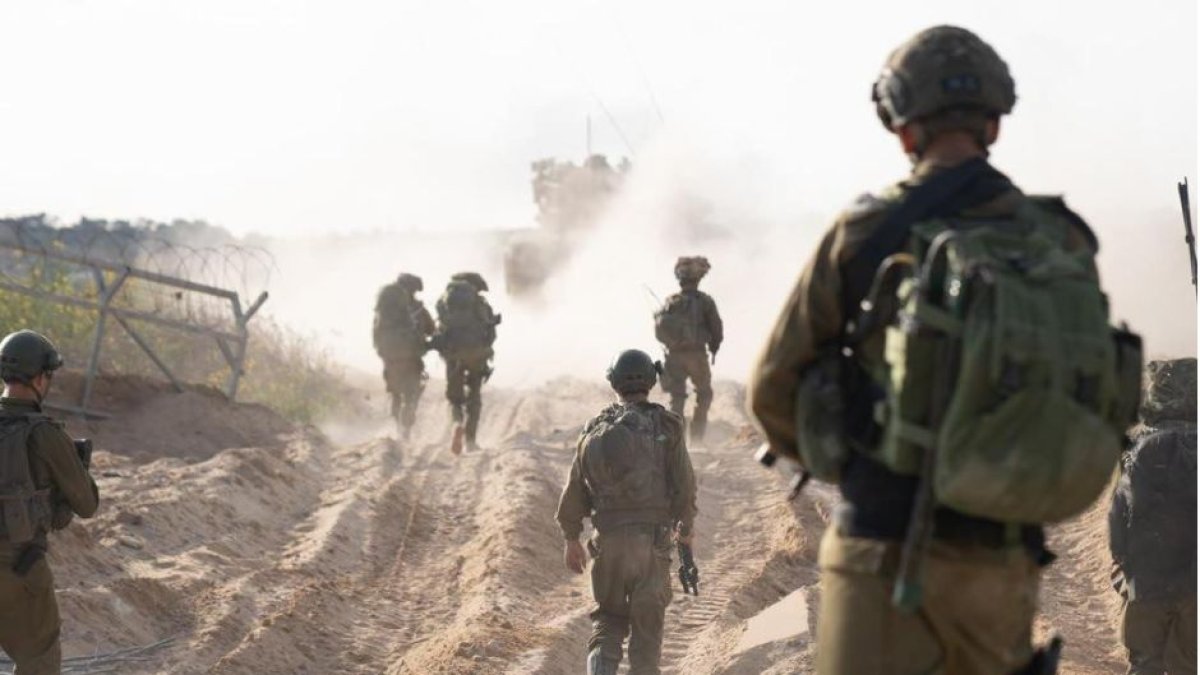 Varios soldados israelíes avanzan hacia Gaza siguiendo un blindado.
