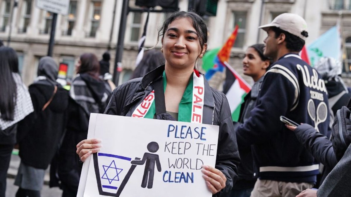 Una manifestante en Londres sostiene un cartel que muestra la bandera de Israel en un tacho de basura con un cartel que dice 