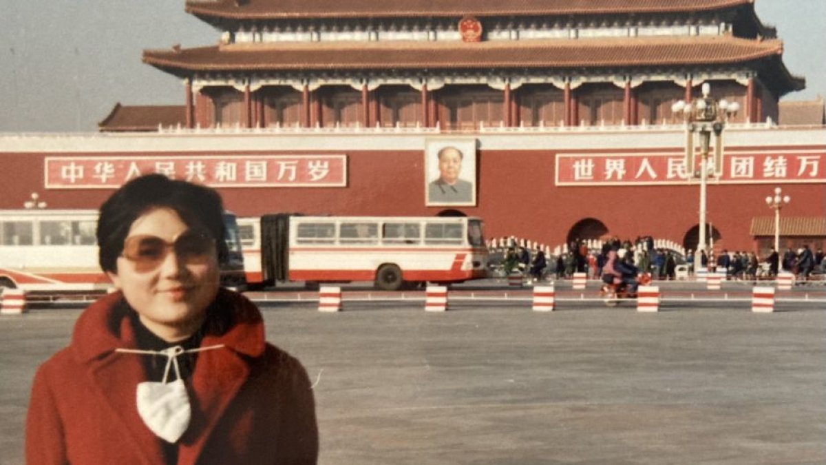 Xi Van Fleet en China frente a un edificio decorado con motivos comunistas, incluyendo una fotografía de Mao Zedong.