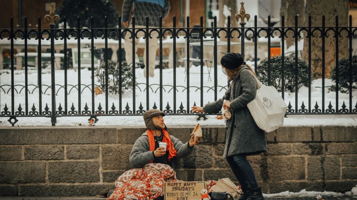 Una mujer entrega una ayuda a un homeless