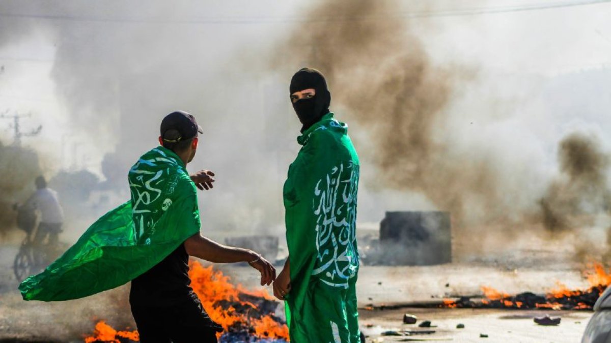 Fotografía de unos manifestantes con la bandera de Hamás que queman neumáticos durante una demostración cerca del puesto de control de Hawwara.