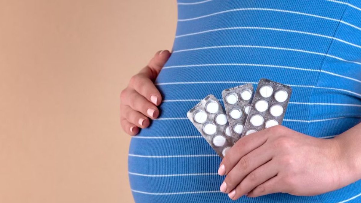 A pregnant woman holds pills in her hand.