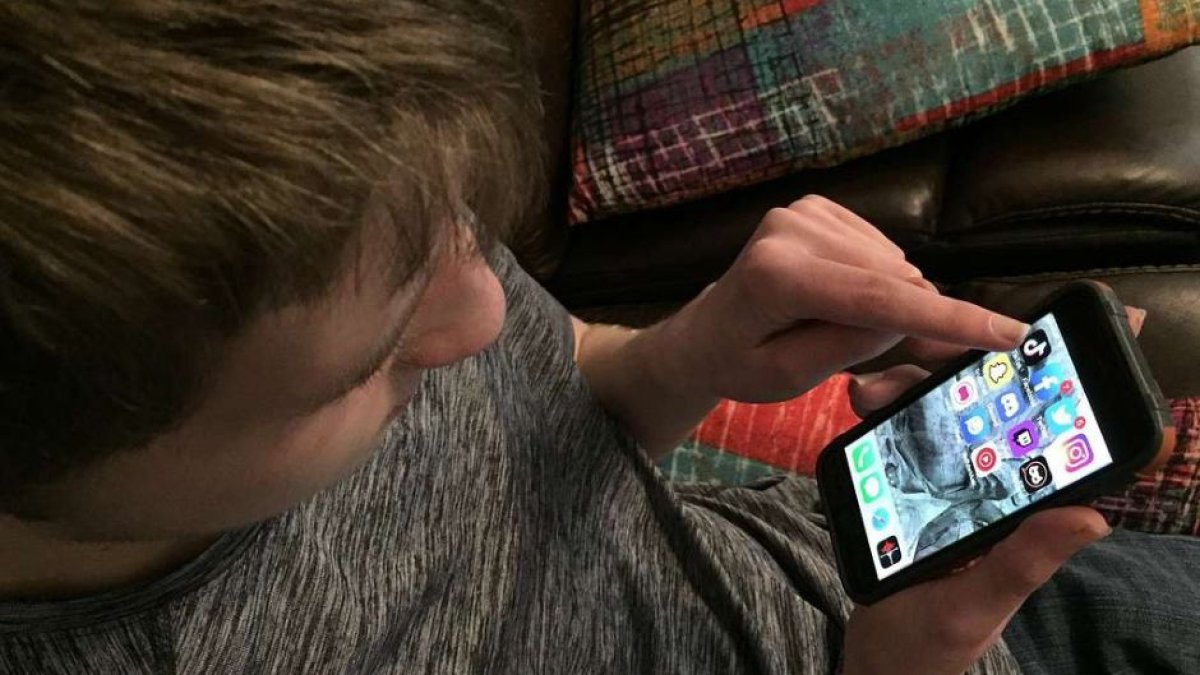 Un joven mirando su pantalla del móvil en busca de entrar en una de las redes sociales en las que tiene cuenta.