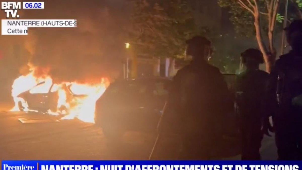 Antidisturbios franceses pasan junto a un coche ardiendo.