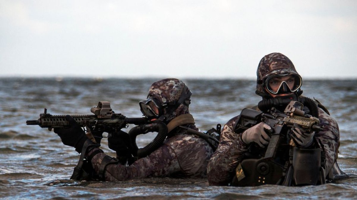 Dos miembros del Navy Seal emergen del agua portando sus rifles.