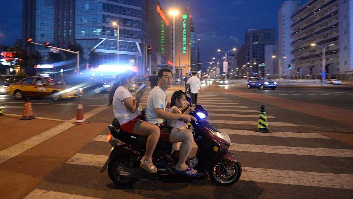 POblación en China. Una pequeña familia circula por las calles de la ciudad montada en una motocicleta de tipo scooter.
