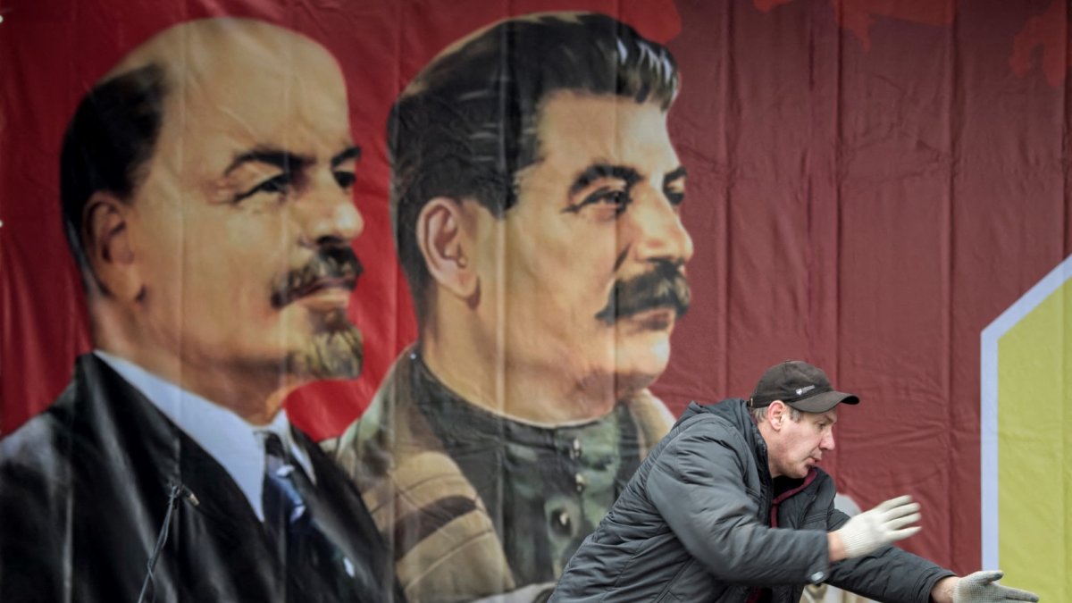 A worker gestures in front of a poster depicting Soviet leaders Vladimir Lenin and Joseph Stalin on a stage erected for events marking the 100th anniversary of The Bolshevik Revolution in downtown Moscow on November 7, 2017. (Photo by Mladen ANTONOV / AFP)
