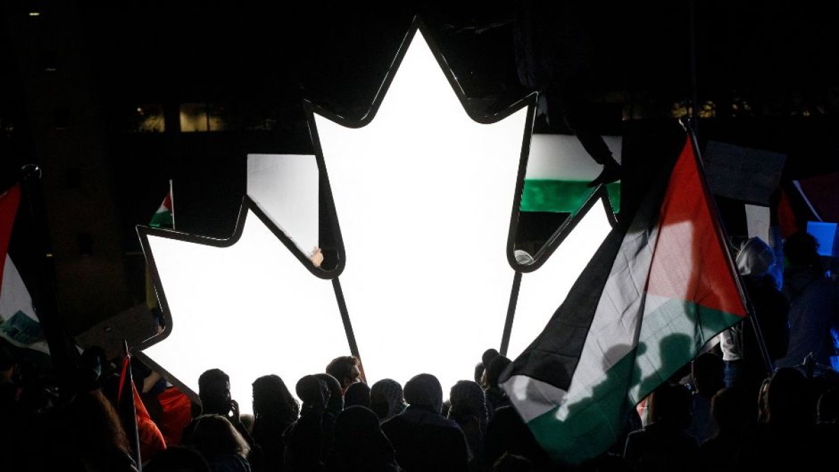 Un grupo de personas junto a una hoja de arce canadiense iluminada mientras miles de personas se reúnen en Toronto (Ontario, Canadá) para mostrar su apoyo a Palestina.