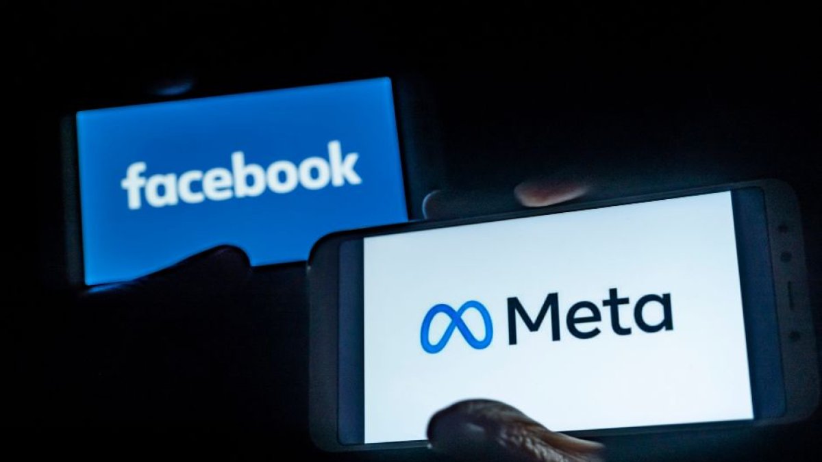 Una mano sosteniendo un móvil en el que se ve el logo de Meta. Detrás, otra mano sosteniendo otro smartphone con el logo de Facebook, la red social propiedad de la Big Tech.