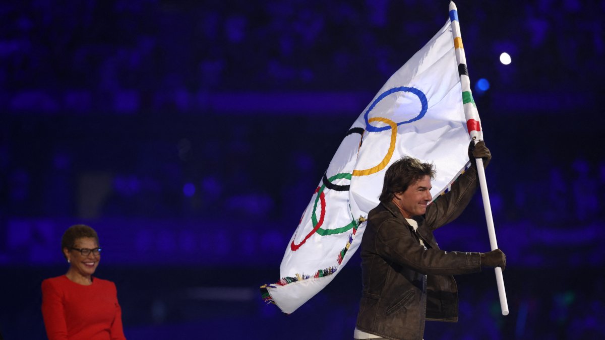 El actor estadounidense Tom Cruise sale con la bandera olímpica ante la alcaldesa de Los Ángeles, Karen Bass