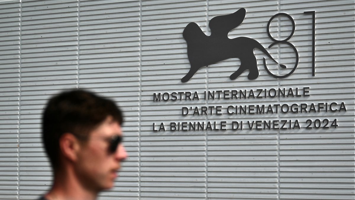 A man walks past the official logo of the 81th Venice Film Festival at Venice Lido, on August 27, 2024 on the eve of the opening ceremony. - With 21 films vying for the top Golden Lion prize, the 81st edition of the prestigious festival kicks off tomorrow, with Lady Gaga, Daniel Craig and Brad Pitt expected on the red carpet during the 10-day affair. (Photo by Marco BERTORELLO / AFP)