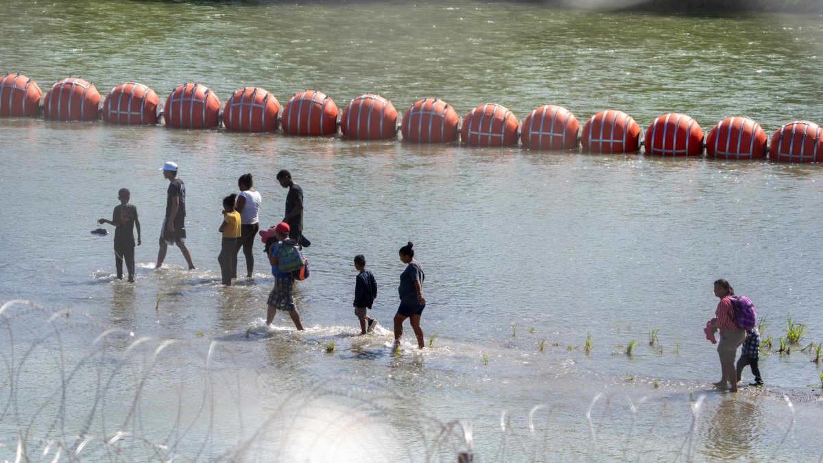 Crisis fronteriza: Migrantes caminan junto a una cadena de boyas colocadas en el agua a lo largo de la frontera del Río Grande con México en Eagle Pass, Texas,