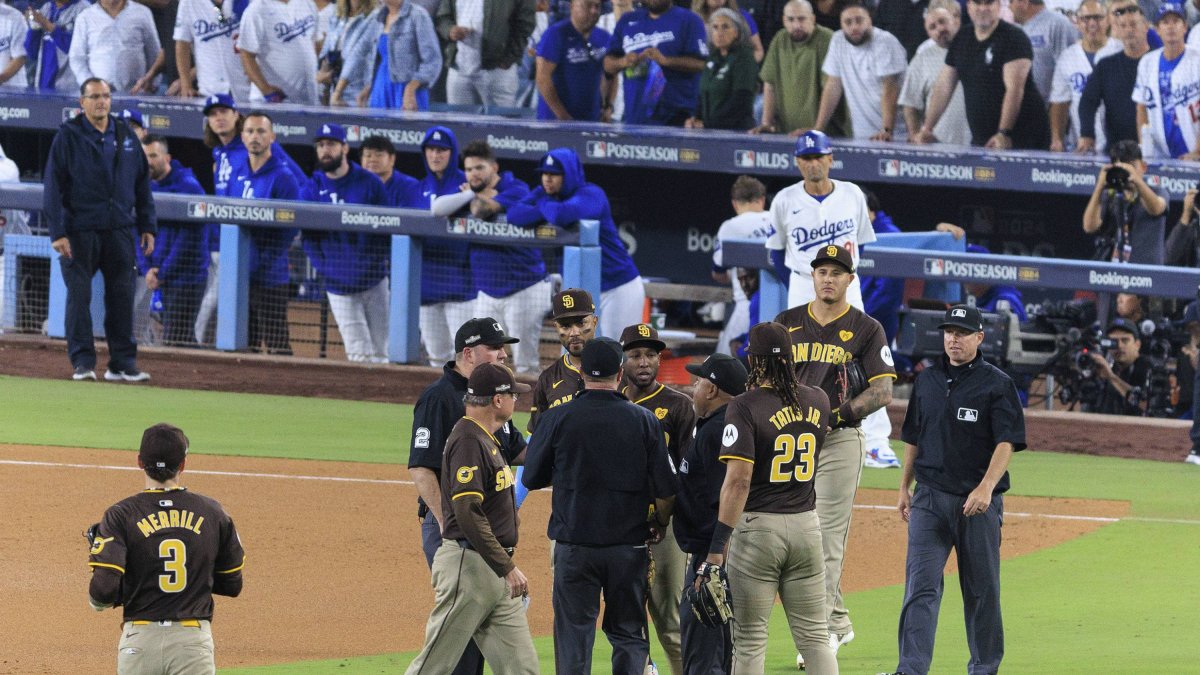 Los jugadores de los Padres de San Diego reciben instrucciones mientras que el Juego 2 de la NLDS del domingo 6 de octubre de 2024 se detiene debido a que los aficionados lanzan basura y pelotas de béisbol al campo en la 7ª entrada del partido entre los Dodgers de Los Ángeles y los Padres de San Diego en el Dodger Stadium de Los Ángeles, California. Jurickson Profar y Fernando Tatis hablan con los árbitros mientras les lanzan pelotas y basura.