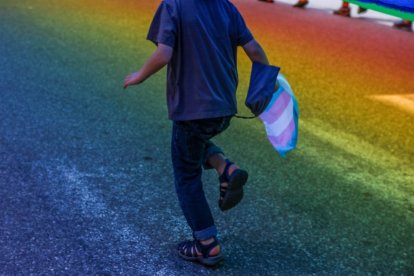 A boy runs with the trans flag in his hand.