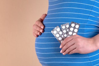 A pregnant woman holds pills in her hand.