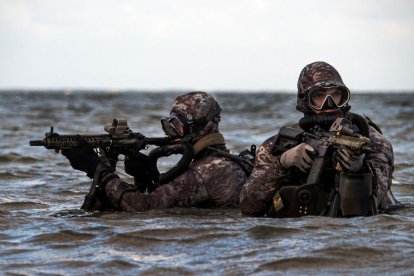 Dos miembros del Navy Seal emergen del agua portando sus rifles.