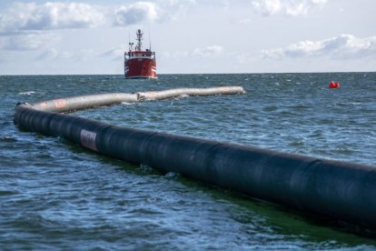 Un barco a la distancia navega. Más cerca, se ve un tubo flotar en el agua.