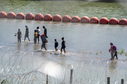 Crisis fronteriza: Migrantes caminan junto a una cadena de boyas colocadas en el agua a lo largo de la frontera del Río Grande con México en Eagle Pass, Texas,