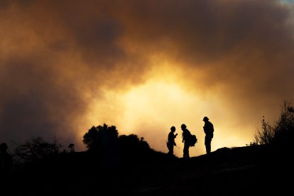 Varios bomberos observan cómo el fuego asciende por las colinas detrás de Pacific Palisades el sábado por la mañana mientras los aviones de extinción de incendios lanzan agua y rellenan para combatir las llamas