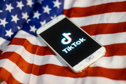 Primer plano del logotipo de TikTok mostrado en la pantalla de un teléfono, smartphone sobre la bandera estadounidense, la bandera nacional de los Estados Unidos.