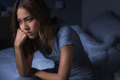 A woman sitting on the edge of her bed unable to fall asleep.
