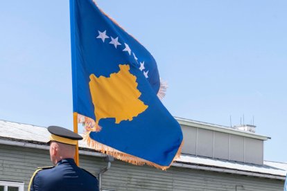 A military man flies the flag of Kosovo