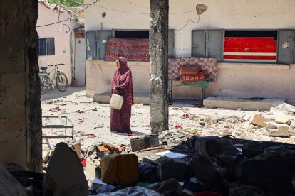 Una mujer sostiene una botella de plástico frente a una escuela destrida en Gaza