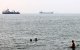 Men bathe in the Gulf waters as vessels in the background transit the Strait of Hormuz off the coast of Iran's southern port city of Bandar Abbas on September 7, 2026. Iran's top negotiator threatened on September 6 of a more forceful response to any further US attacks after Tehran targeted American warships in their latest round of clashes. The exchanges of fire, which began with US raids last week, come amid a deadlock in the six-month war between the two foes. (Photo by ATTA KENARE / AFP) /