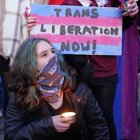 Activista trans con la cara cubierta por una bandana sostiene una vela delante de un cartel que reza "Liberación trans ahora".