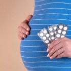 A pregnant woman holds pills in her hand.
