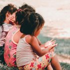 Tres niñas de espaldas sentadas en un parque.