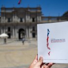 Fotografía de una mano sosteniendo un libreto con la segunda propuesta constitucional para modificar la Constitución de Chile delante del palacio presidencial.