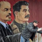 A worker gestures in front of a poster depicting Soviet leaders Vladimir Lenin and Joseph Stalin on a stage erected for events marking the 100th anniversary of The Bolshevik Revolution in downtown Moscow on November 7, 2017. (Photo by Mladen ANTONOV / AFP)