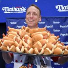 Joey Chestnut, el campeón de comer perritos calientes, sujeta una bandeja repleta de perritos.